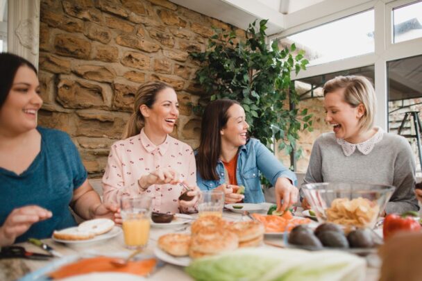 Vier vriendinnen zitten aan tafel te kletsen en lachen.