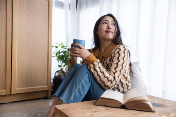 Vrouw zit met een kopje thee bij een raam en kijkt naar buiten.