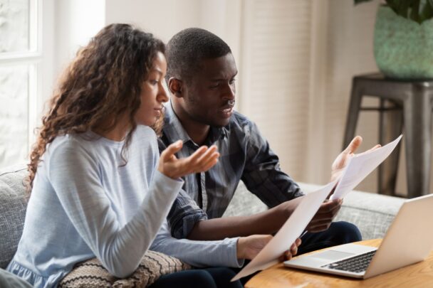 Man en vrouw bekijken samen papieren en gebruiken een laptop. Ze ogen wat gespannen.