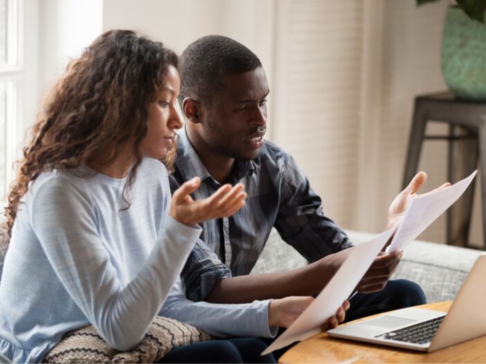 Man en vrouw bekijken samen papieren en gebruiken een laptop. Ze ogen wat gespannen.