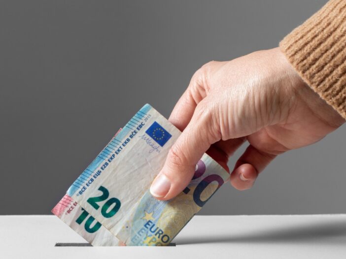 Hand stopt twee biljetten van 20 en 10 euro in een spaarpot.