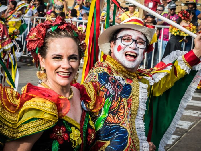 Man en vrouw in kleurrijke carnavalskleding kijken blij de camera in.