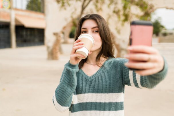 Meisje met to-go koffiebeker in haar hand maakt een selfie.