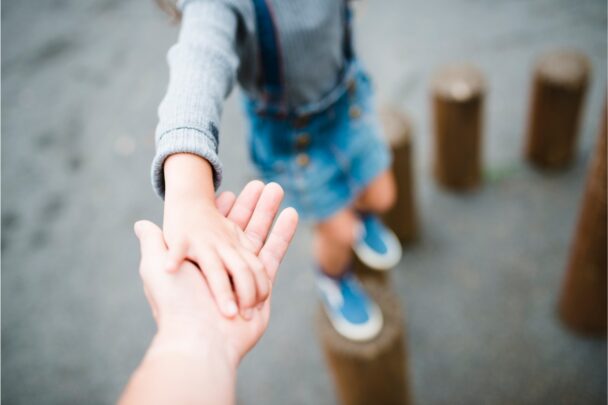 Kind balanceert op houten blokken en houdt daarbij de hand van een volwassene vast.