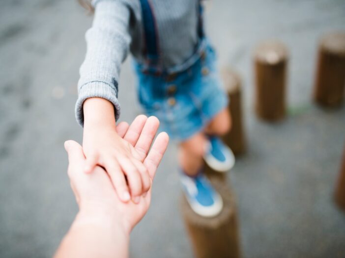 Kind balanceert op houten blokken en houdt daarbij de hand van een volwassene vast.