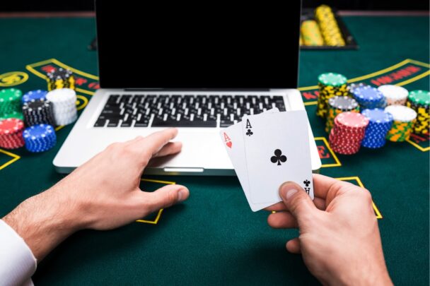 Pokertafel met daarop fiches, een laptop en iemand die twee speelkaarten in zijn handen houdt.