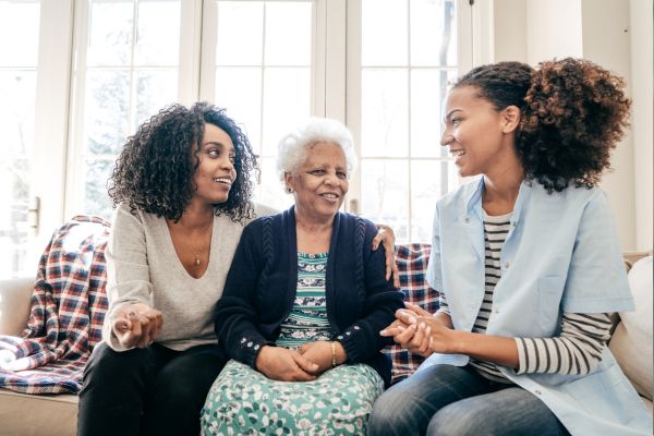 Oudere vrouw zit met twee vrouwen op de bank.