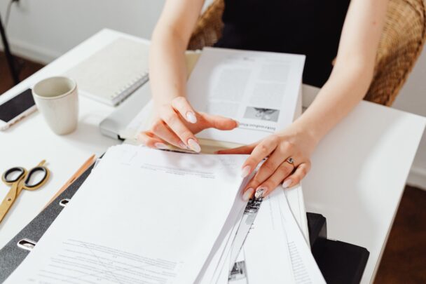 Vrouw bekijkt stapels met papierwerk op een bureau.