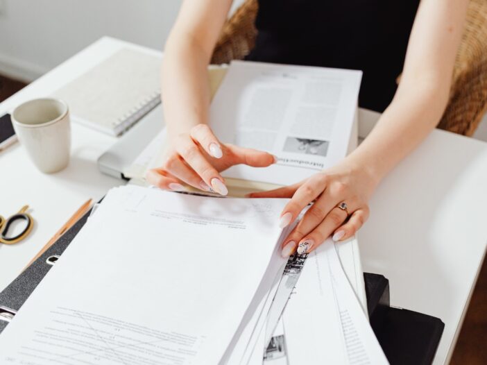 Vrouw bekijkt stapels met papierwerk op een bureau.