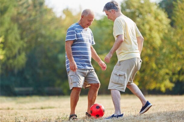 Twee oudere mannen spelen met een voetbal op een grasveld.