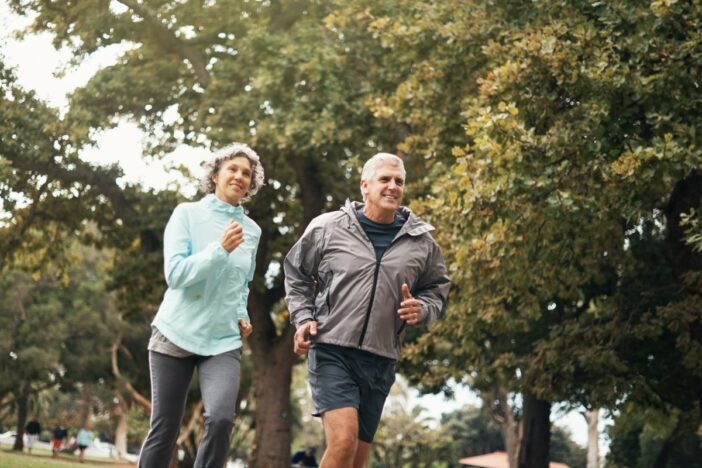 Oudere man en vrouw joggen samen door een bos.