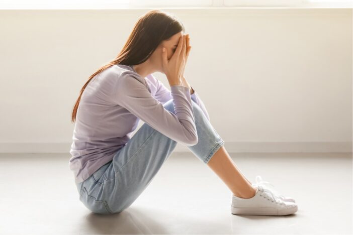 Vrouw zit op de grond met haar handen voor haar gezicht. Ze oogt van streek.